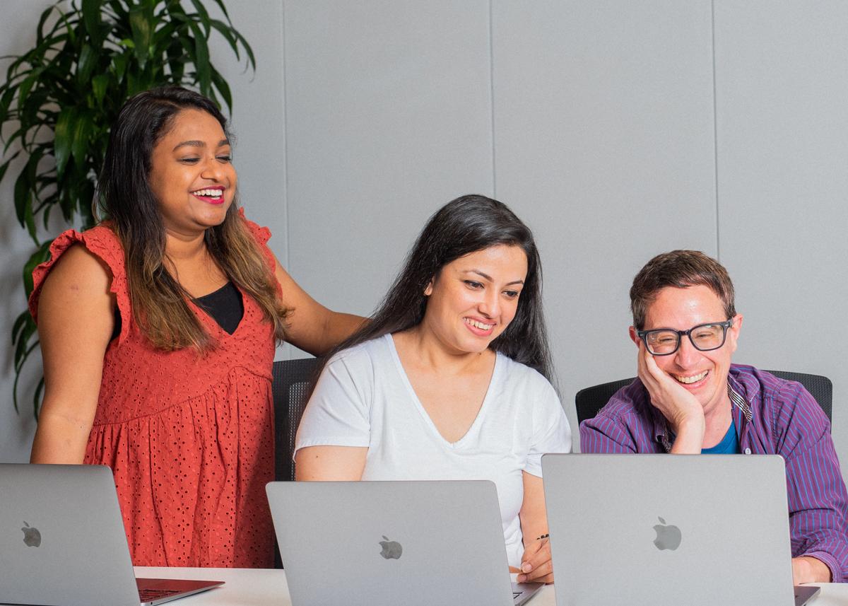 Three people with laptops are smiling and talking